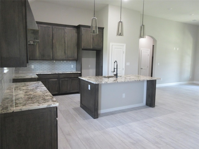 kitchen featuring backsplash, decorative light fixtures, light stone counters, and an island with sink