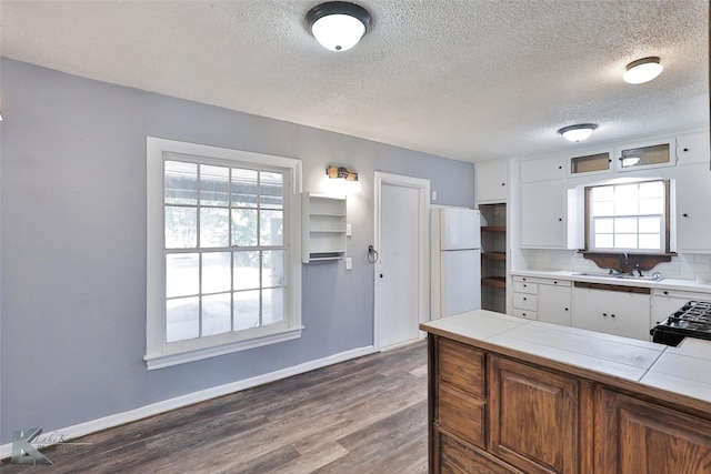 kitchen featuring tile countertops, white cabinetry, sink, white refrigerator, and dark wood-type flooring