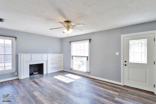 unfurnished living room with dark hardwood / wood-style flooring, a textured ceiling, a fireplace, and ceiling fan