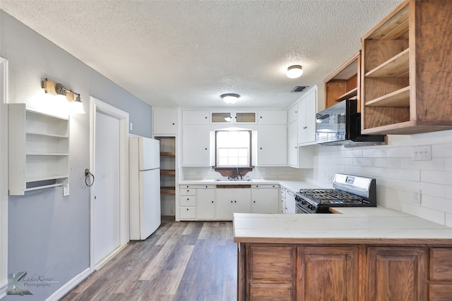 kitchen featuring white cabinetry, kitchen peninsula, backsplash, black appliances, and wood-type flooring