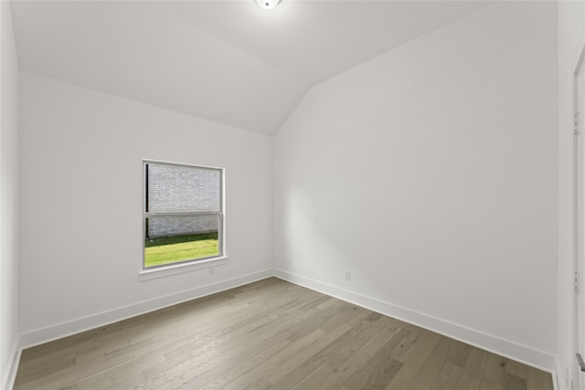 spare room featuring vaulted ceiling, wood finished floors, and baseboards
