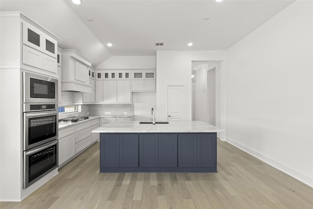 kitchen featuring a sink, white cabinets, a kitchen island with sink, light wood-type flooring, and appliances with stainless steel finishes