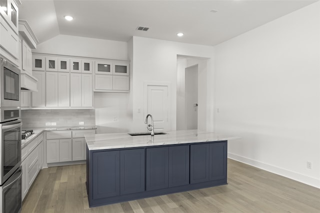kitchen with white cabinets, light wood-type flooring, light stone counters, and a sink