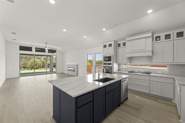 kitchen featuring a sink, tasteful backsplash, open floor plan, a stone fireplace, and appliances with stainless steel finishes