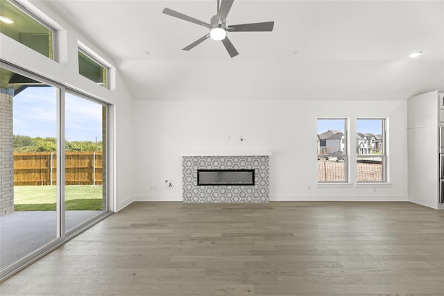 unfurnished living room featuring a ceiling fan, vaulted ceiling, baseboards, a tiled fireplace, and wood finished floors