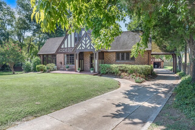 english style home with concrete driveway, a front lawn, a carport, and brick siding