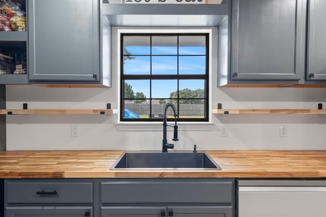 kitchen featuring gray cabinets, dishwasher, wooden counters, and sink