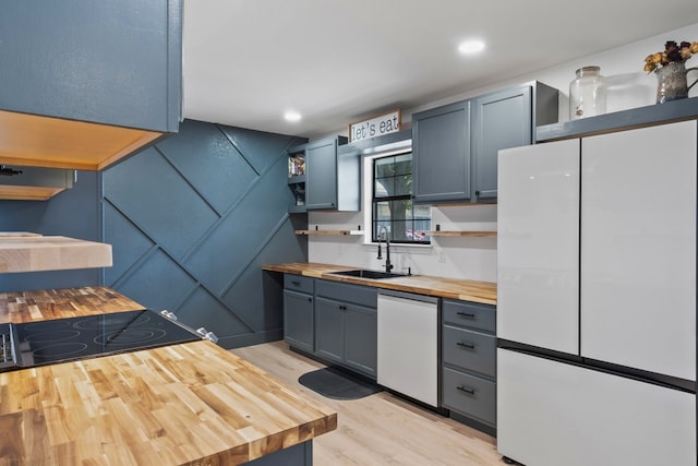 kitchen with dishwasher, white refrigerator, butcher block counters, light hardwood / wood-style floors, and sink