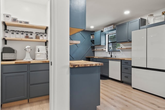 kitchen featuring light hardwood / wood-style floors, butcher block countertops, blue cabinetry, white appliances, and sink