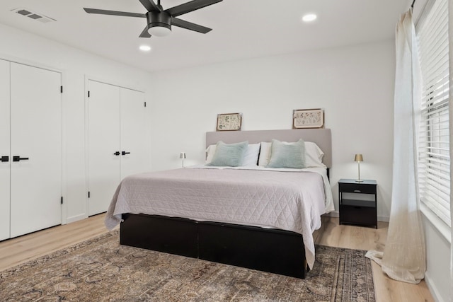 bedroom featuring ceiling fan, multiple windows, multiple closets, and light wood-type flooring