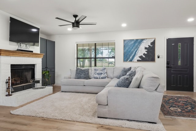 living room with ceiling fan, a brick fireplace, and light hardwood / wood-style flooring