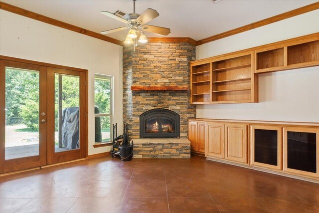 unfurnished living room with ceiling fan, ornamental molding, french doors, a stone fireplace, and dark tile patterned flooring