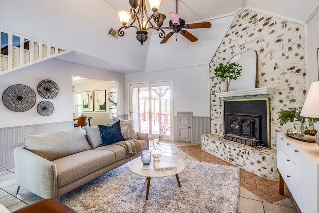 tiled living room featuring ceiling fan with notable chandelier, a wood stove, crown molding, and vaulted ceiling