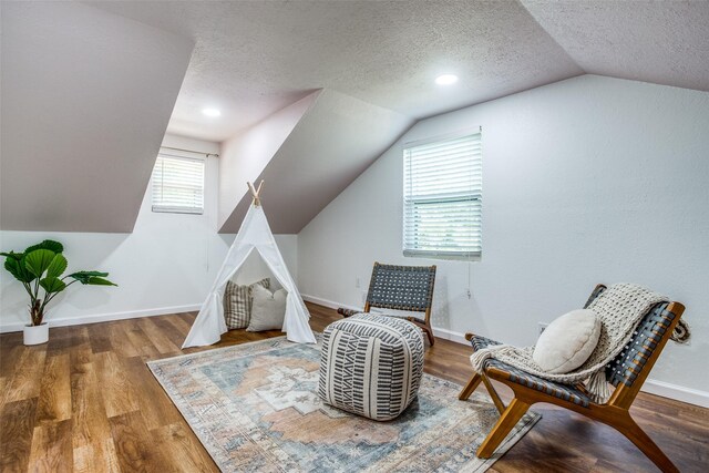 living area with wood-type flooring, a textured ceiling, a wealth of natural light, and vaulted ceiling