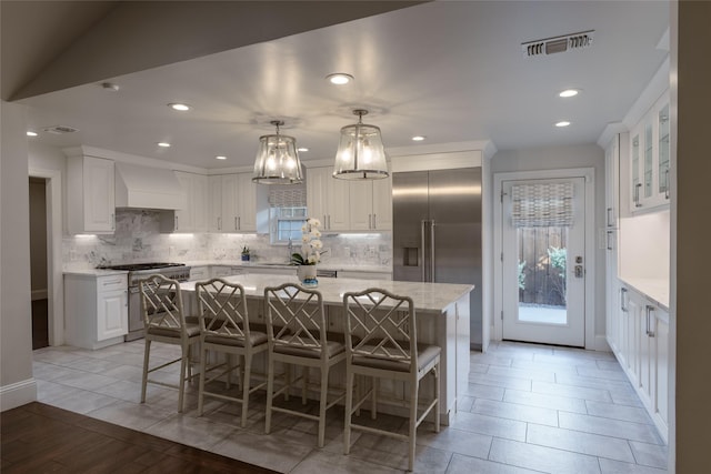 kitchen featuring decorative light fixtures, high end appliances, white cabinetry, and a center island