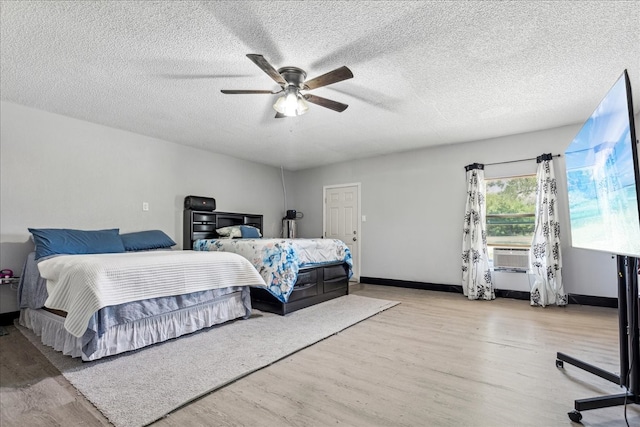 bedroom featuring cooling unit, a textured ceiling, ceiling fan, and light hardwood / wood-style flooring