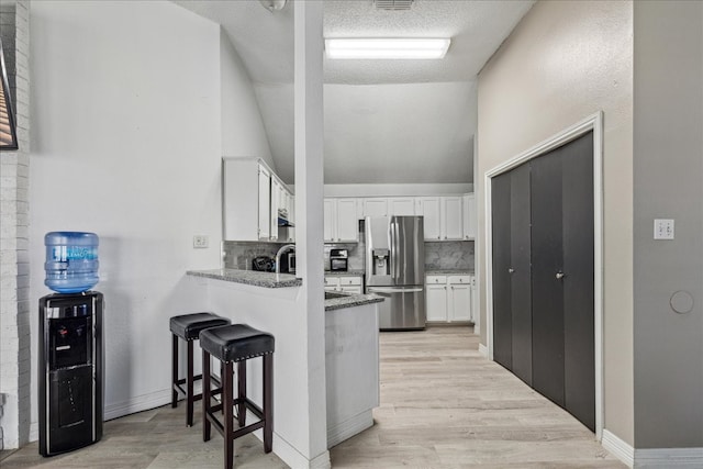 kitchen featuring stainless steel fridge, a kitchen bar, decorative backsplash, stone countertops, and white cabinetry