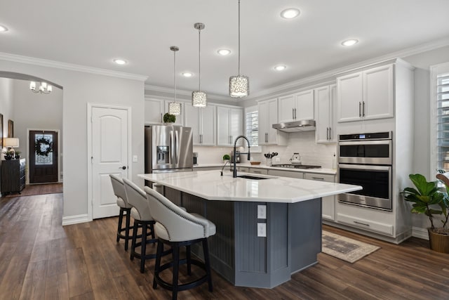 kitchen with pendant lighting, sink, white cabinets, stainless steel appliances, and a center island with sink