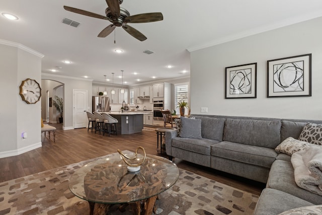 living room featuring ceiling fan, sink, dark wood-type flooring, and ornamental molding