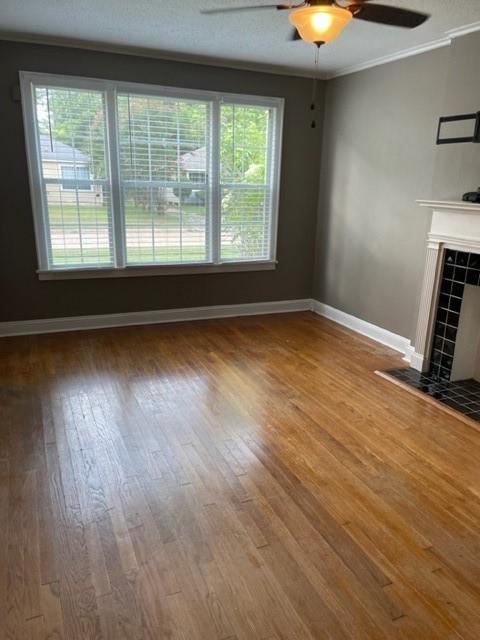 unfurnished living room with a tiled fireplace, ceiling fan, a healthy amount of sunlight, and wood-type flooring