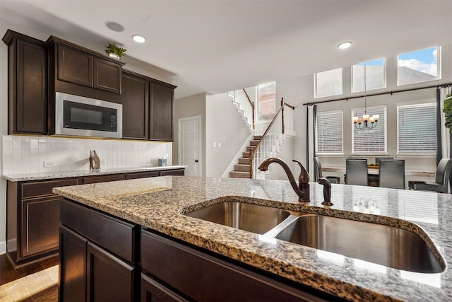 kitchen featuring light stone countertops, sink, backsplash, a chandelier, and built in microwave