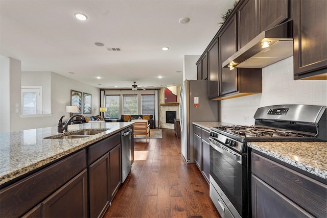 kitchen with range hood, sink, a tiled fireplace, dark wood-type flooring, and appliances with stainless steel finishes