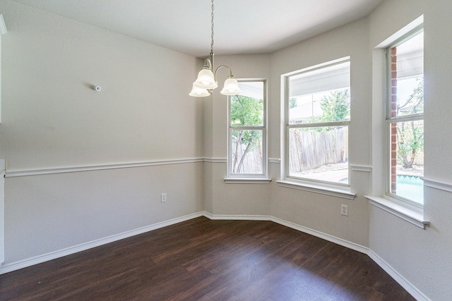 empty room with dark wood-type flooring, plenty of natural light, and a chandelier