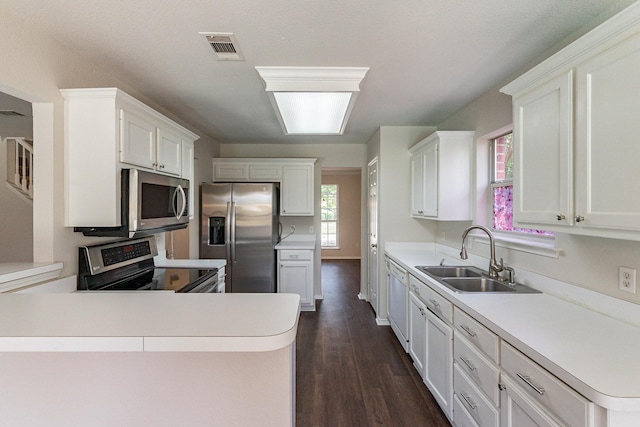 kitchen with sink, dark wood-type flooring, appliances with stainless steel finishes, white cabinets, and kitchen peninsula