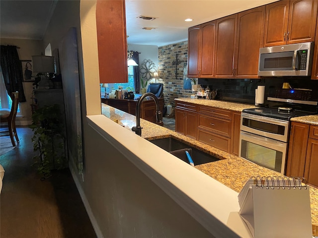 kitchen featuring appliances with stainless steel finishes, hardwood / wood-style floors, sink, light stone counters, and backsplash