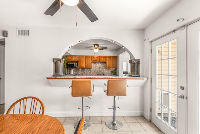 kitchen featuring kitchen peninsula, backsplash, light tile patterned flooring, and ceiling fan