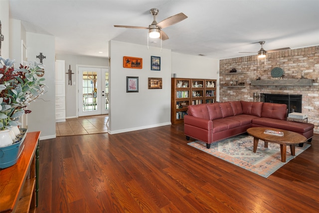 living room with brick wall, wood-type flooring, a brick fireplace, and ceiling fan