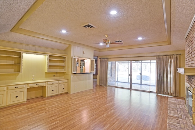 unfurnished living room featuring a fireplace, built in desk, a raised ceiling, light hardwood / wood-style flooring, and a textured ceiling