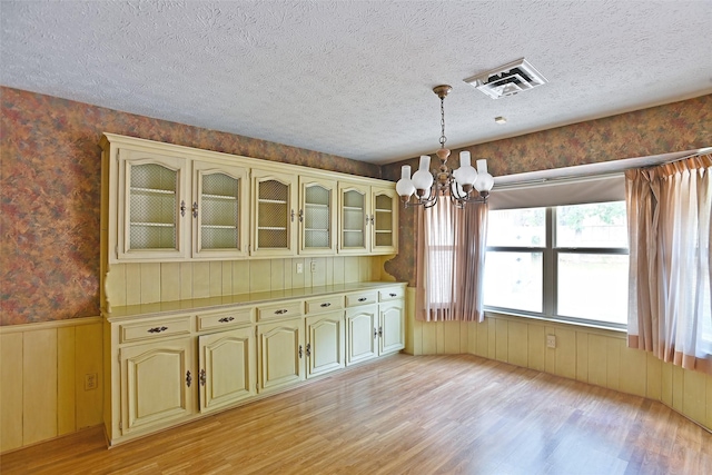 unfurnished dining area featuring light hardwood / wood-style floors, a textured ceiling, and a notable chandelier