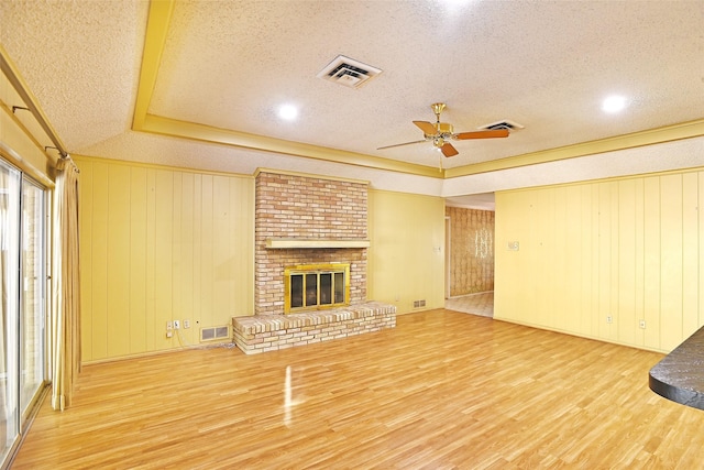 unfurnished living room featuring wood walls, hardwood / wood-style floors, a brick fireplace, ceiling fan, and a textured ceiling