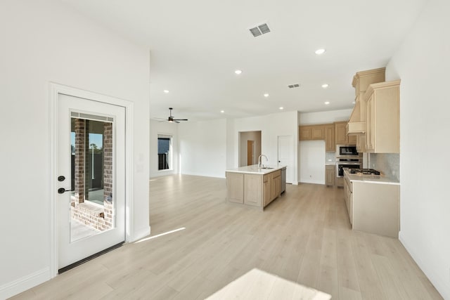 kitchen featuring built in microwave, sink, oven, light hardwood / wood-style floors, and a center island with sink