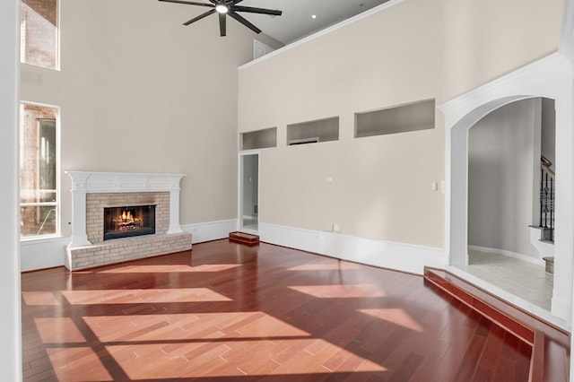 unfurnished living room with a brick fireplace, a towering ceiling, hardwood / wood-style floors, and ceiling fan