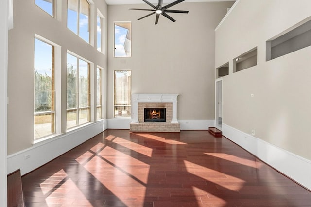 unfurnished living room with a towering ceiling, plenty of natural light, a fireplace, and dark hardwood / wood-style flooring