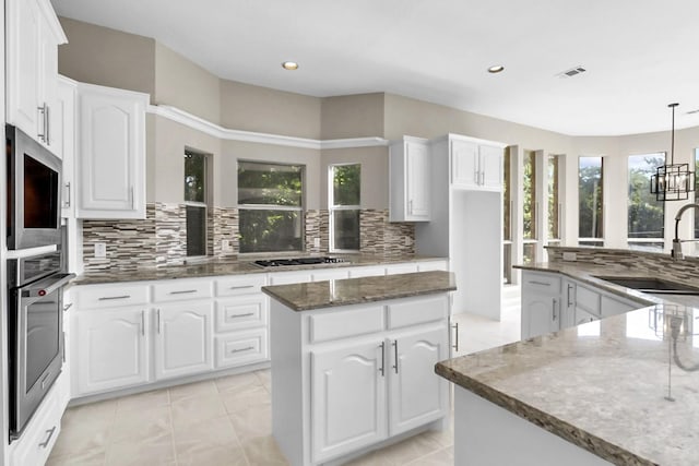 kitchen featuring sink, tasteful backsplash, hanging light fixtures, a kitchen island, and white cabinets