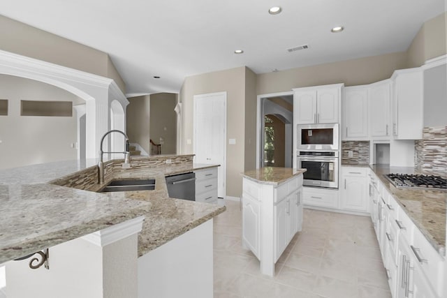 kitchen featuring appliances with stainless steel finishes, tasteful backsplash, white cabinets, a center island, and light stone counters