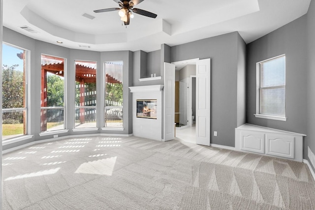 unfurnished living room with light colored carpet, ceiling fan, and a tray ceiling