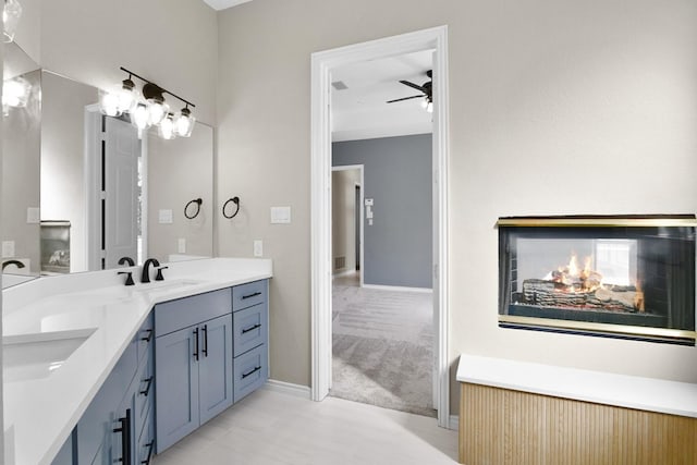 bathroom featuring a multi sided fireplace, vanity, and ceiling fan