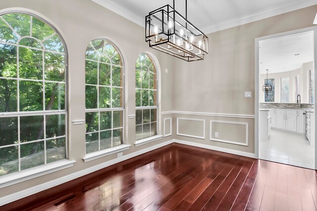 unfurnished dining area with ornamental molding, sink, hardwood / wood-style floors, and a chandelier