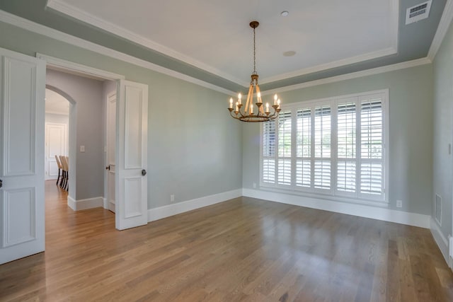 empty room featuring an inviting chandelier, wood-type flooring, crown molding, and a tray ceiling