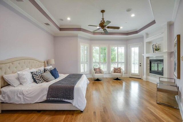 bedroom with ornamental molding, ceiling fan, light wood-type flooring, and a tray ceiling