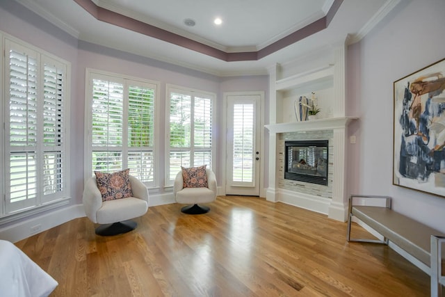 living area with a tray ceiling, light wood-type flooring, and a multi sided fireplace