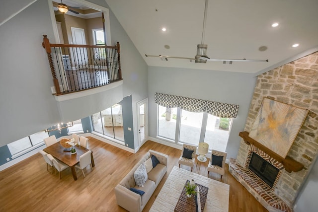 living room featuring high vaulted ceiling, a fireplace, light wood-type flooring, and ceiling fan