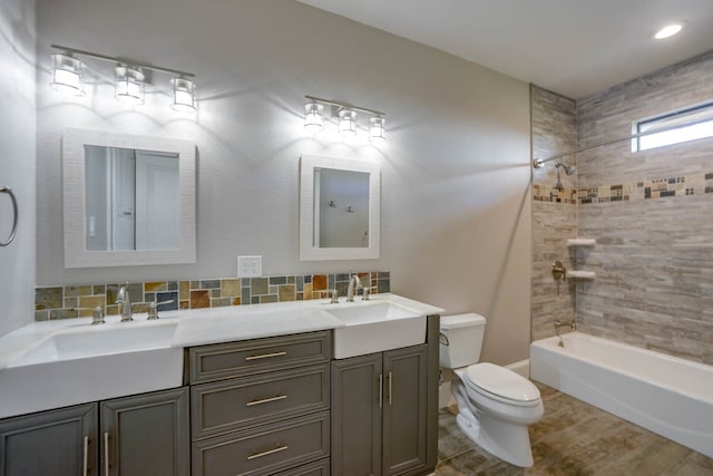 full bathroom with hardwood / wood-style flooring, tasteful backsplash, tiled shower / bath, dual vanity, and toilet