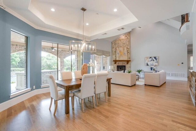 dining room featuring a stone fireplace, light hardwood / wood-style flooring, a wealth of natural light, and a tray ceiling