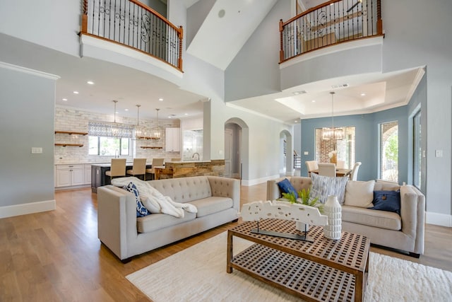 living room featuring crown molding, a towering ceiling, light wood-type flooring, and a chandelier