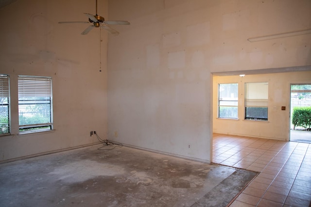 tiled spare room featuring a wealth of natural light, ceiling fan, and a high ceiling